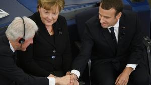 Bill Clinton ściska dłoń Emmanuela Macrona, między nimi Angela Merkel